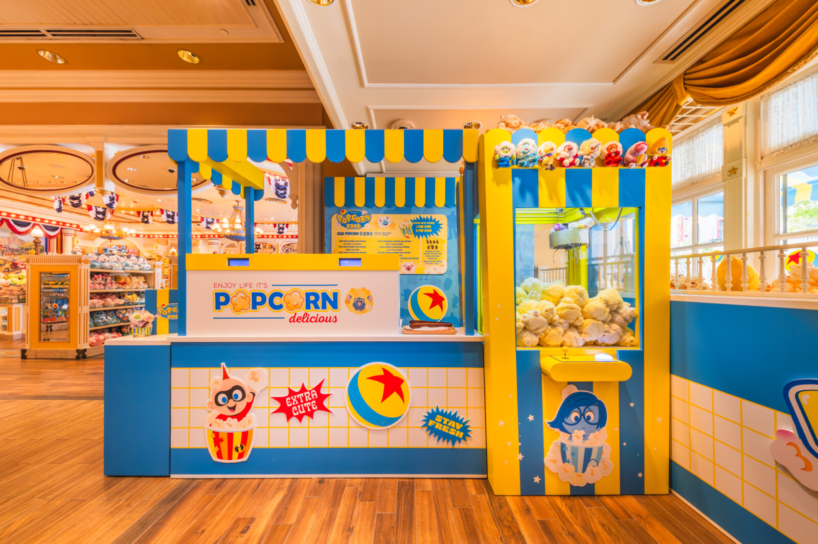 香港ディズニーランド・メインストリートのポップコーンポップアップショップ。ピクサーキャラクターをあしらったブルー×イエローの装飾とクレーンゲーム機が並ぶ店内