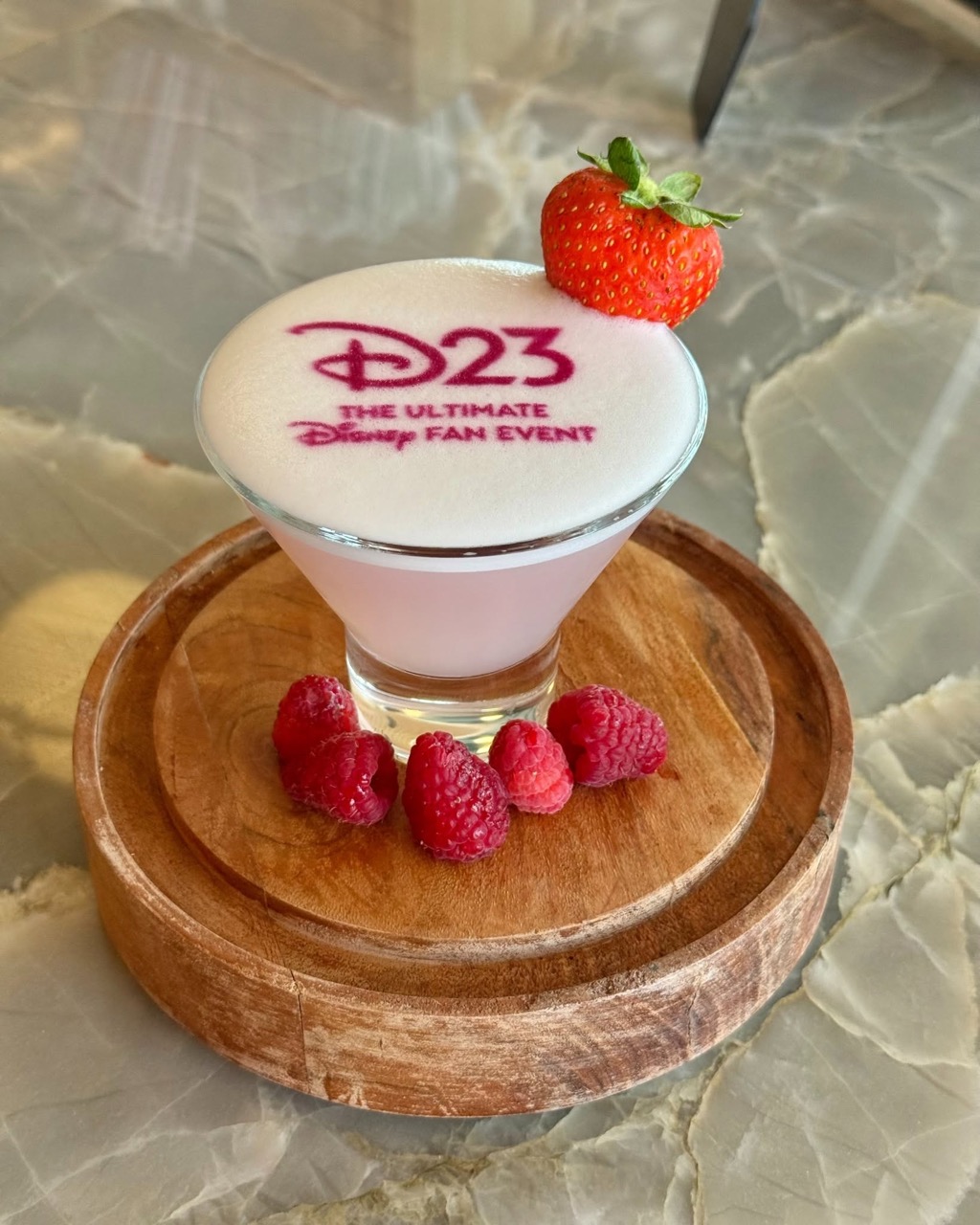 D23ロゴをフォームにあしらった淡いピンクのマティーニ系カクテル