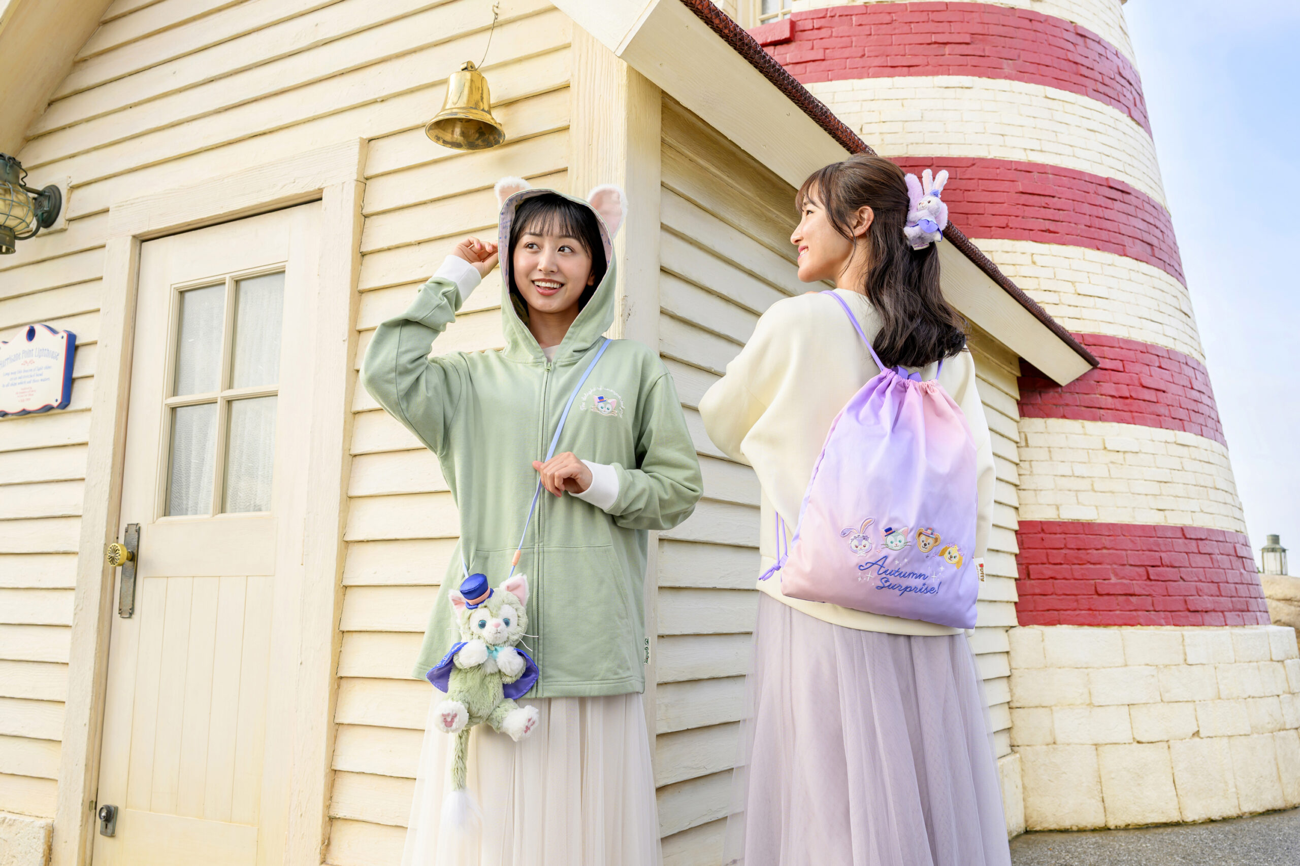 灯台前でジェラトーニ耳付きパーカーとAutumn Surprise!の巾着リュックを身につけた女性2人