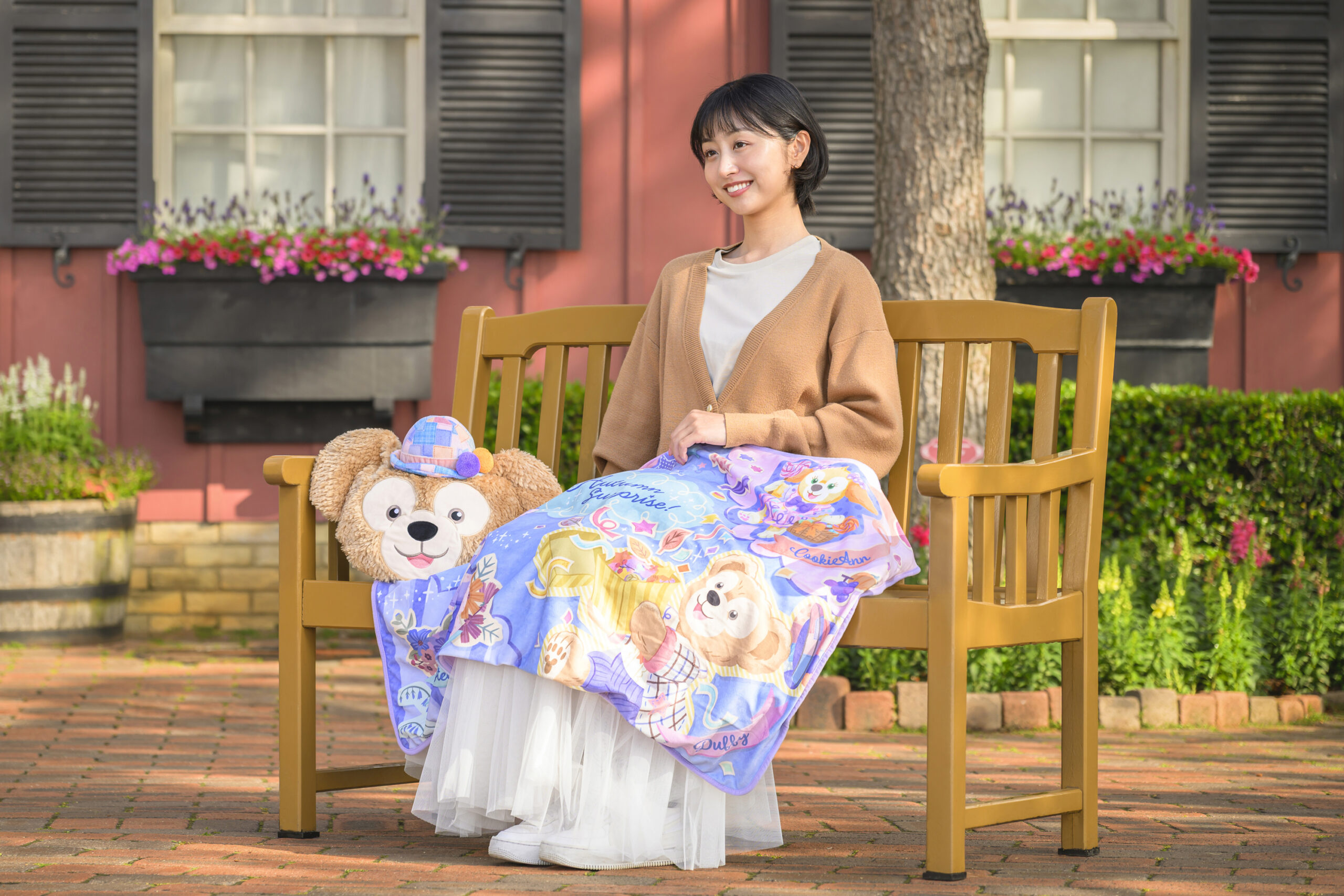ベンチでダッフィーの収納ケース付きブランケットを広げる女性とダッフィーのぬいぐるみ